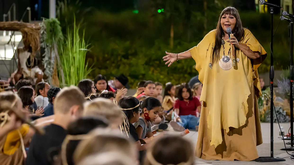 A woman speaking on stage to a crowd of people at CSUSB on California Native American Day