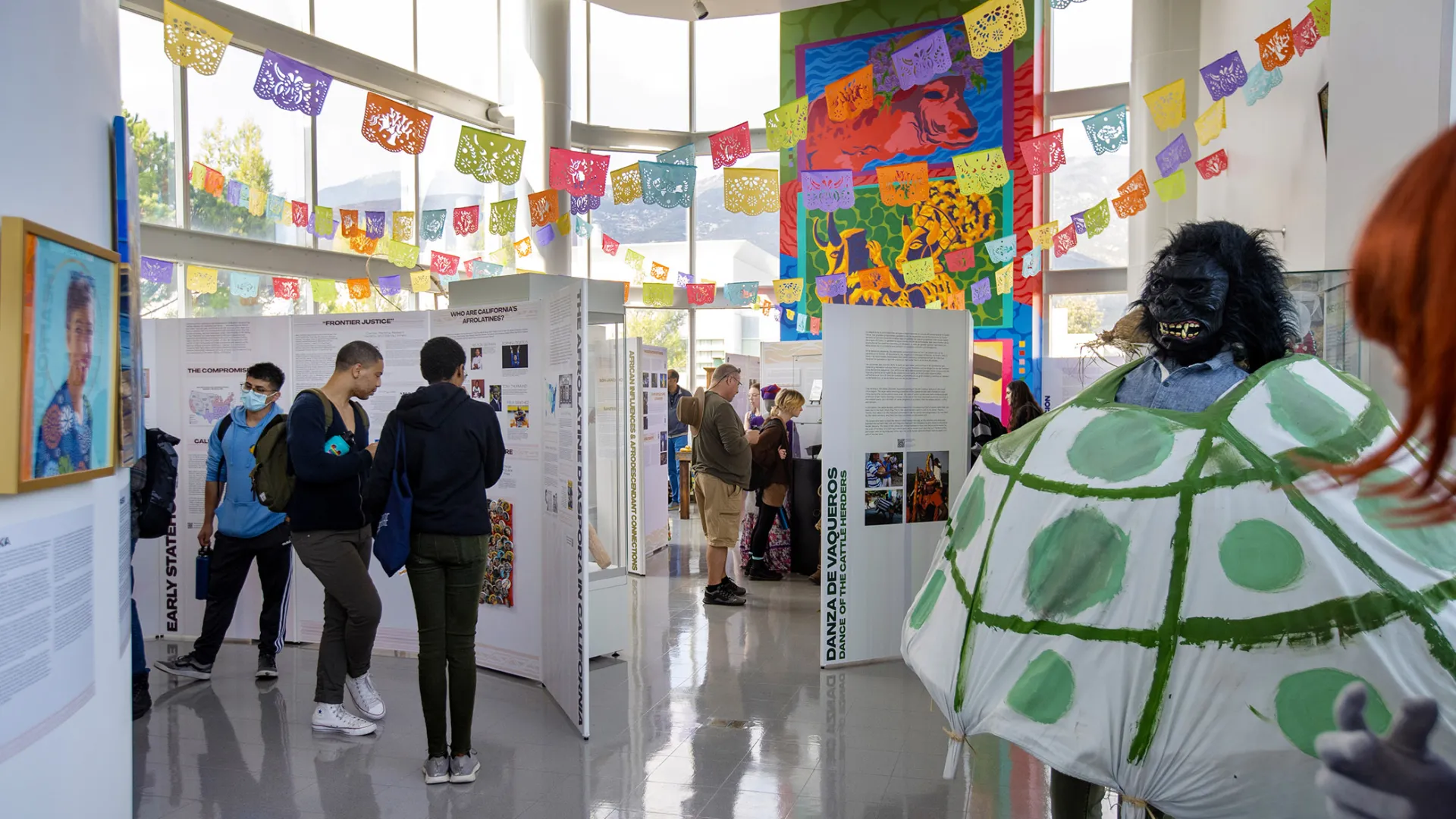 Visitors make their way through the Afróntalo exhibition at CSUSB’s Anthropology Museum. Rising up on the wall is the two-story mural painted by Julio “Honter” Antuna Lopez, and to the left is a prop for the Danza de la Tortuga (Dance of the Turtle) from Mexico’s Costa Chica region.