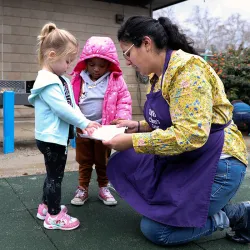 An educator outside the CSUSB Children’s Center speaking to two young children