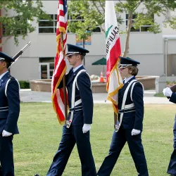 Four people in uniform march across the CSUSB lawn