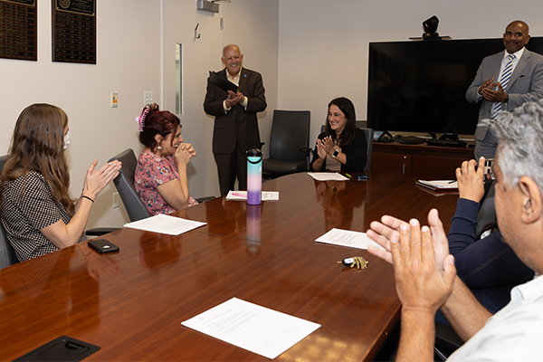 CSUSB President Tomás D. Morales presenting the 2023-24 Golden Apple Award to Manijee Badiee, professor of psychology, in front of a room filled with fellow faculty members, staff and administrators.