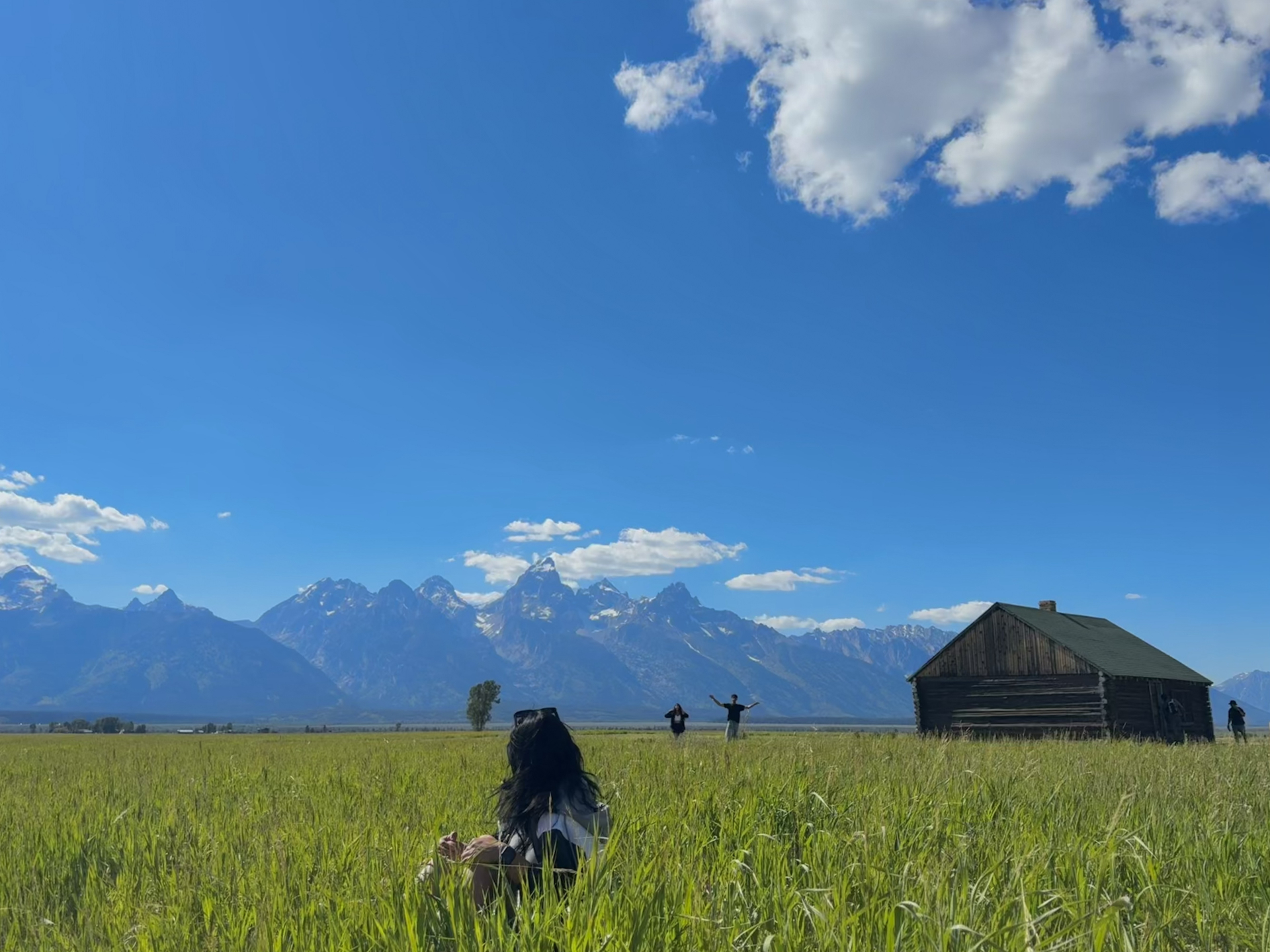 3 people in grass field in with grand teton in background