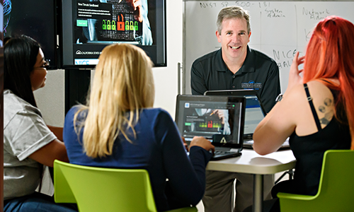 group of students at a table looking at a professor on a TV screen